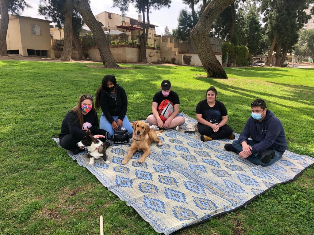 מפגש קבוצתי בטבע הכולל משתתפים וכלבים כחלק מפעילות טיפולית לשיפור מיומנויות חברתיות.